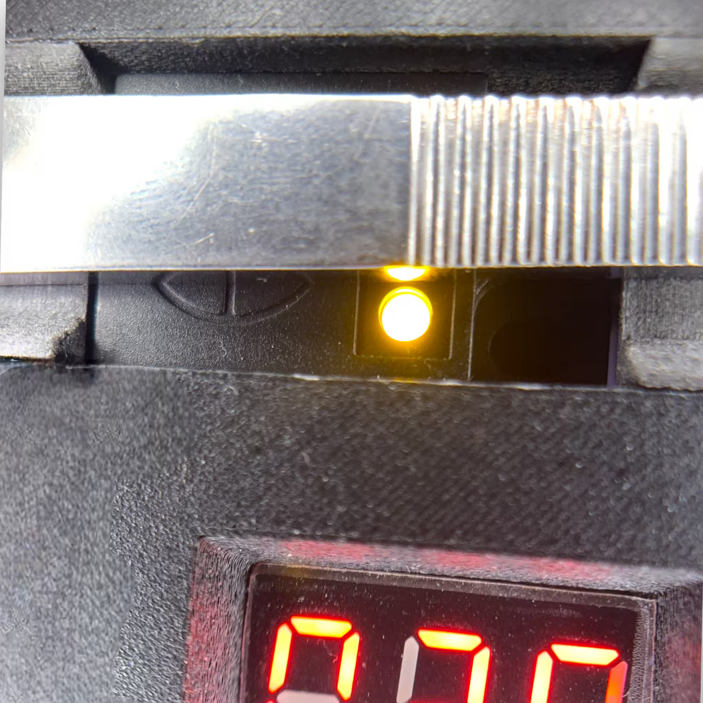 Close-up of a automatic induction sterilizer's active proximity sensor with a glowing yellow light and red LED display.